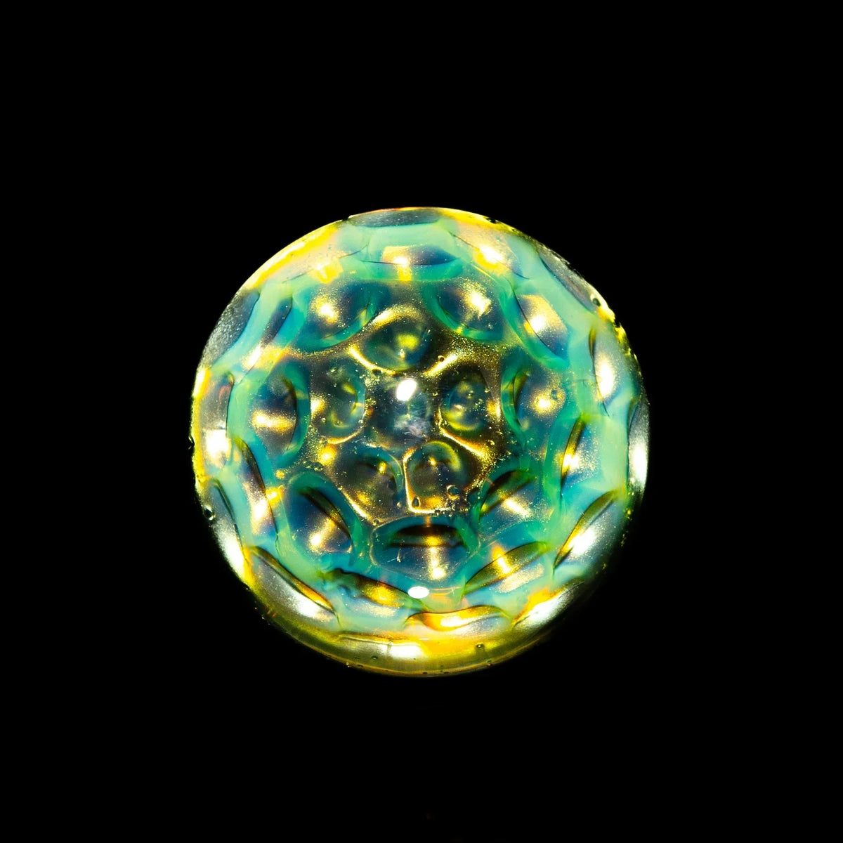 Handblown glass marble with blue and yellow honeycomb pattern on black background