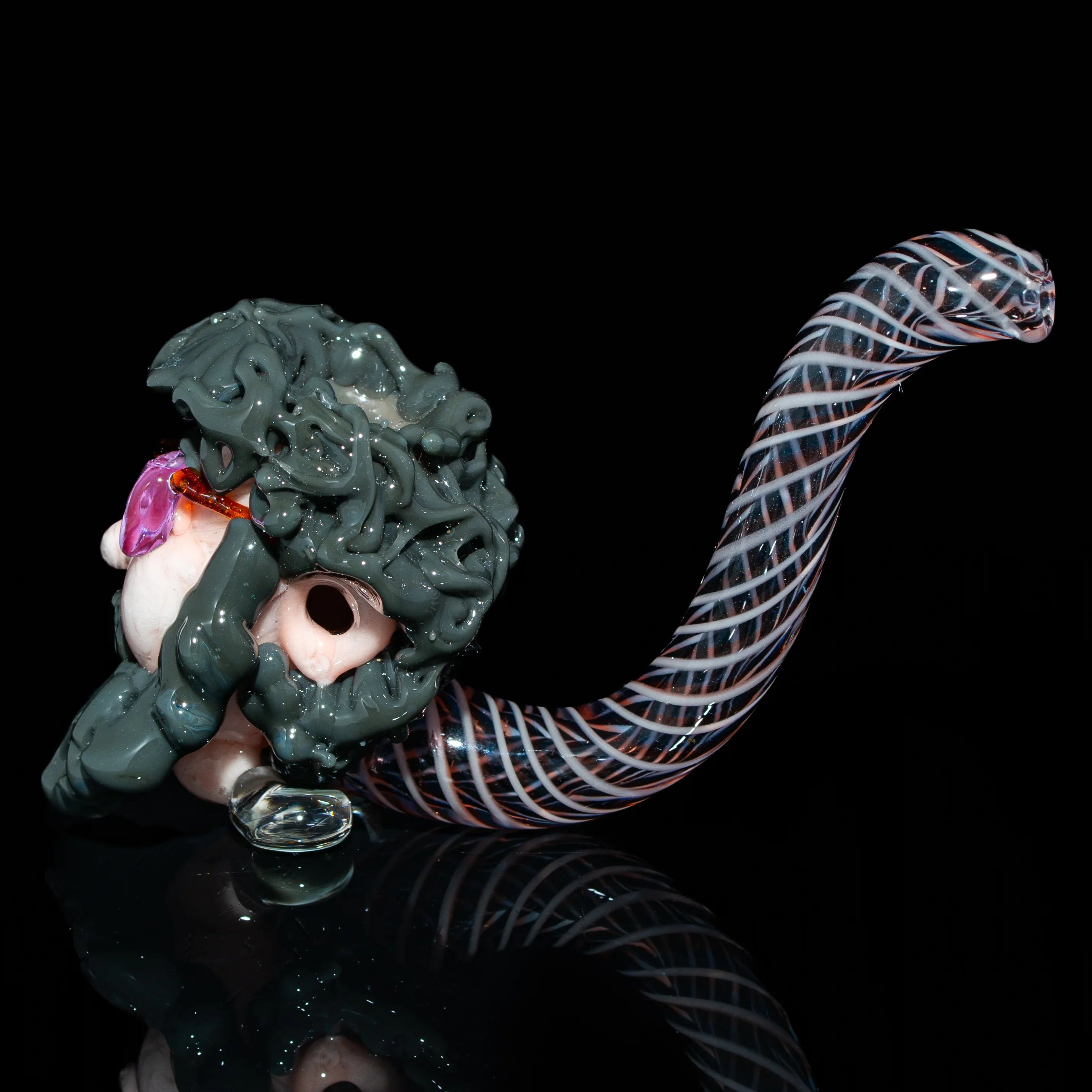 Hand-blown glass pipe with detailed sculpted face and spiral patterned stem on black background