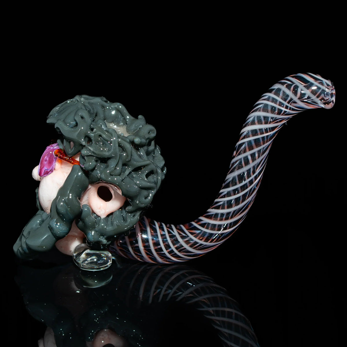 Hand-blown glass pipe with detailed sculpted face and spiral patterned stem on black background