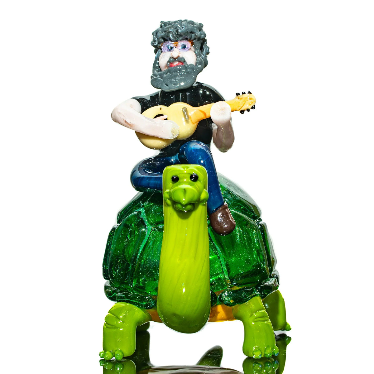 Handcrafted glass art figure of a man with a guitar riding a green turtle on white background