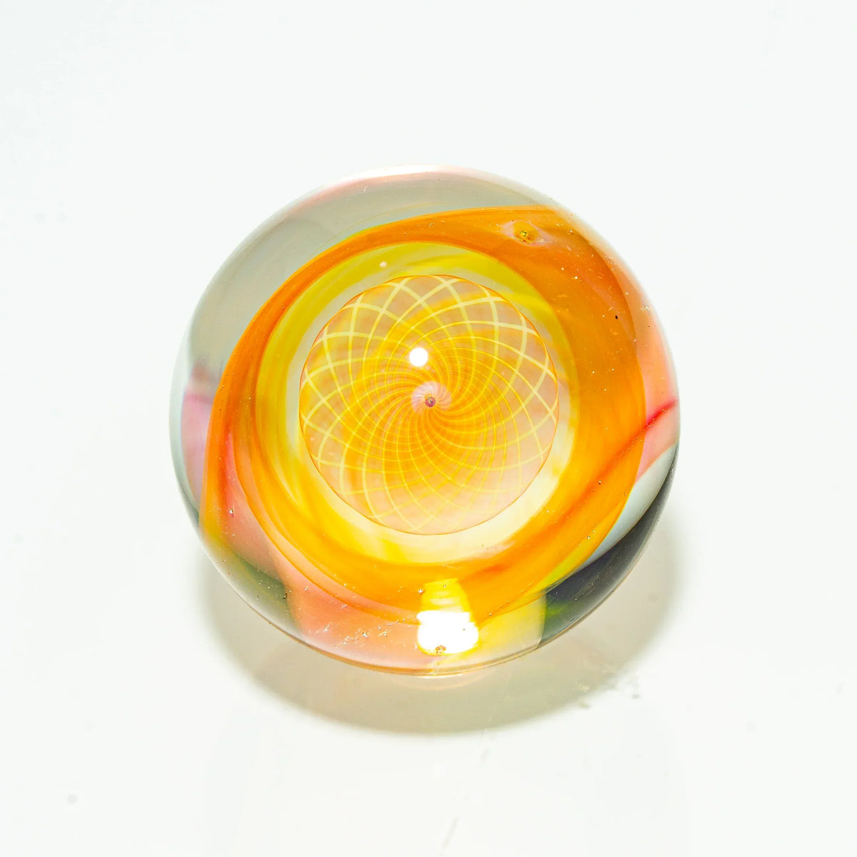 Handcrafted glass marble with vibrant orange and yellow spiral design on white background