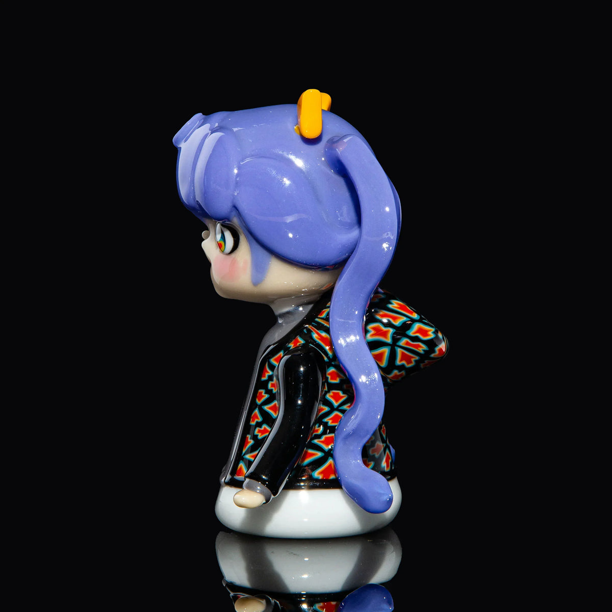 Handcrafted glass art figure with purple hair and patterned jacket on black background