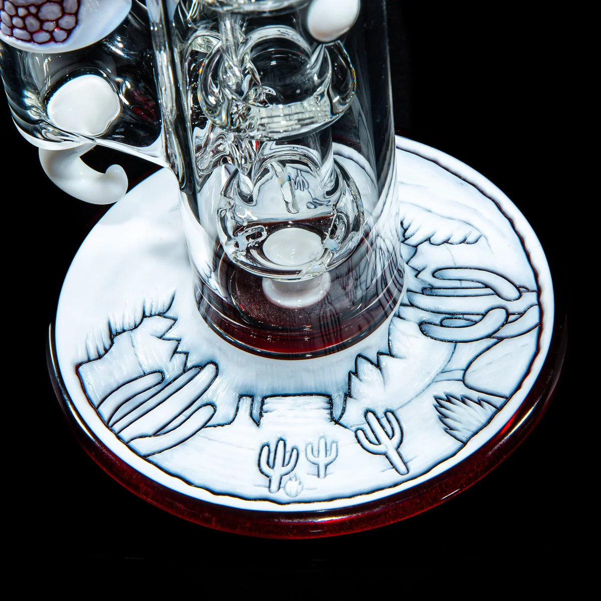 Close-up of artistic glass water pipe base with etched desert landscape and cacti design