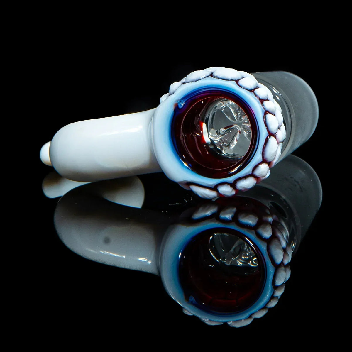 Handmade glass bowl piece with white, red, and blue accents on black reflective surface