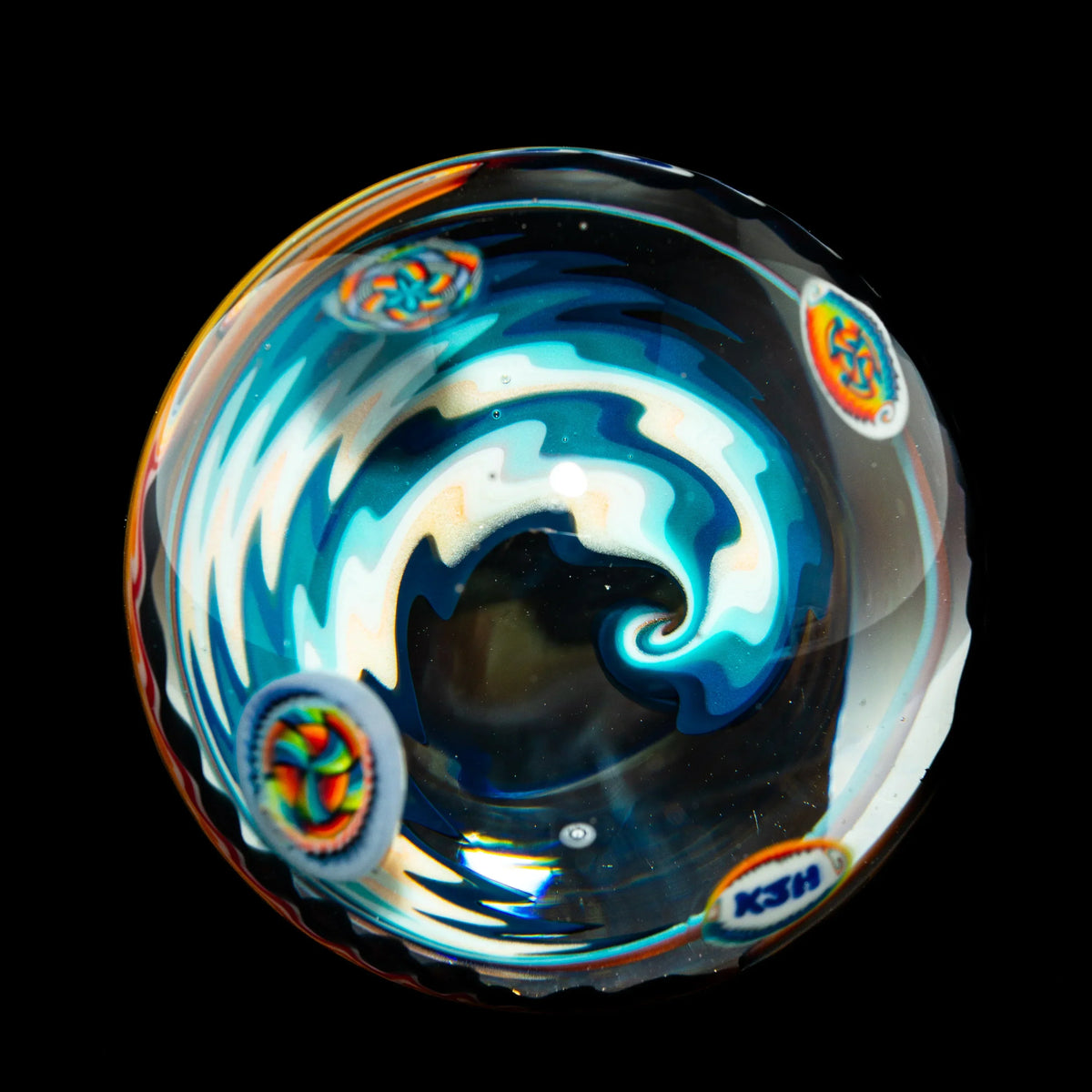 Handcrafted glass marble with vibrant blue and rainbow wave design on black background
