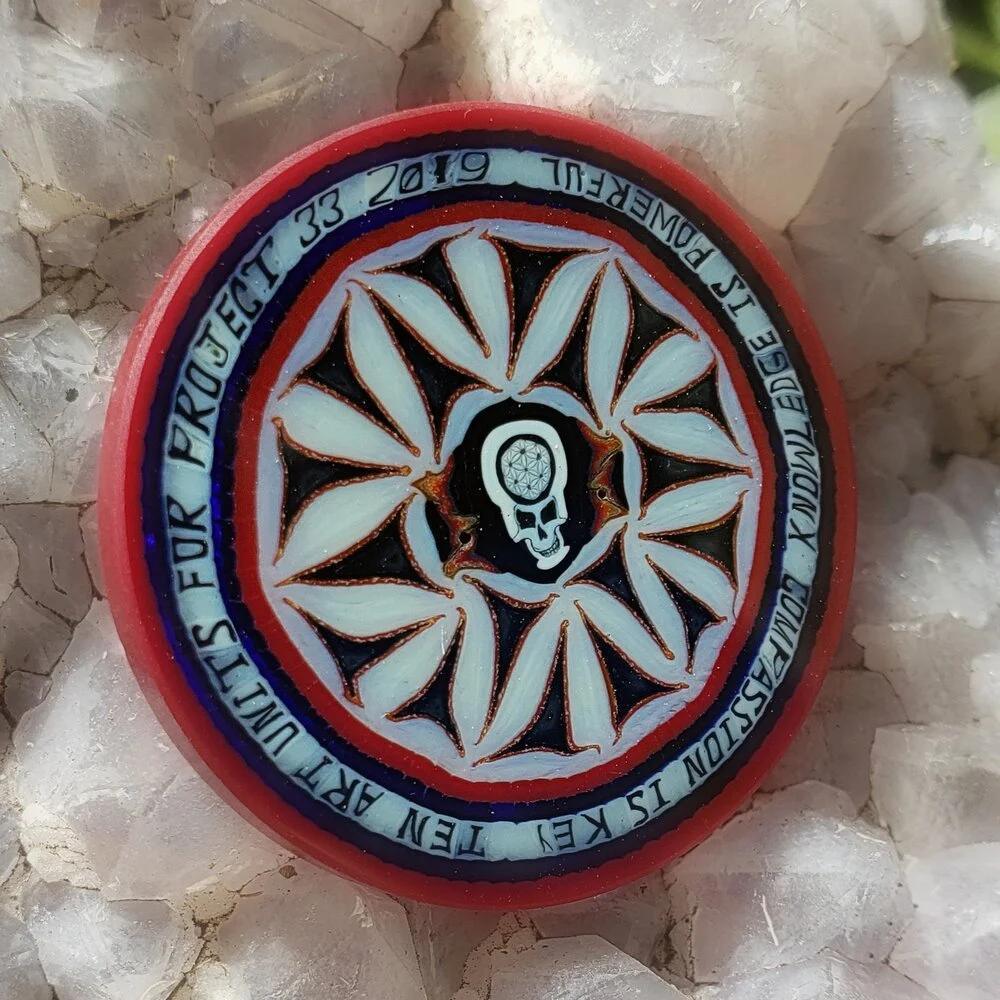 Colorful round glass coin with geometric leaf pattern and skull design, on crystal background.