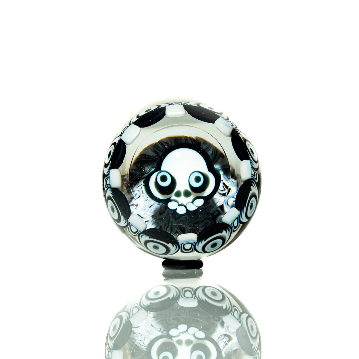 Black and white glass marble with skull design and circular pattern, displayed on reflective surface