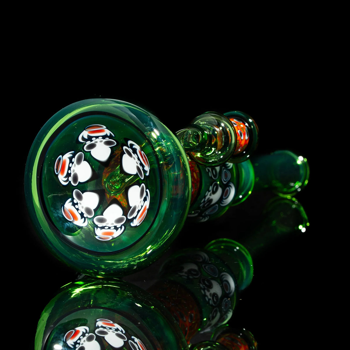 Green glass pipe with intricate mushroom designs, reflected on a black surface