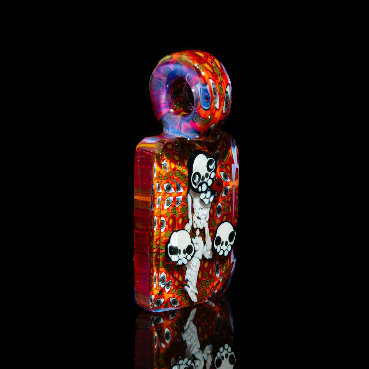 Colorful glass art pendant with skull designs and detailed eye patterns on black background