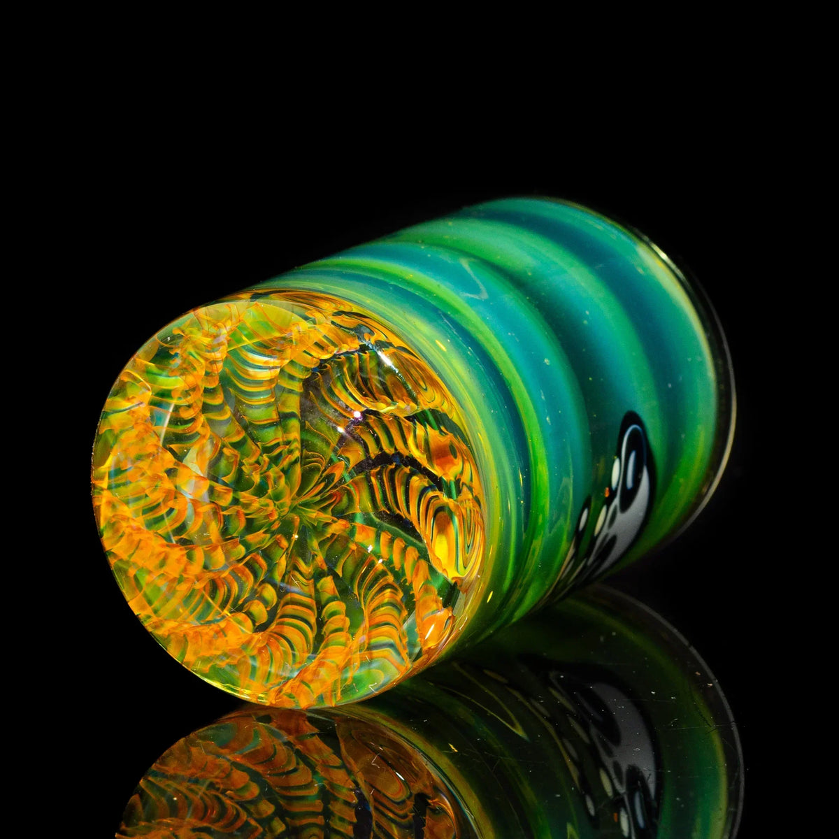 Colorful hand-blown glass cup with green, yellow, and orange spiral pattern on black background
