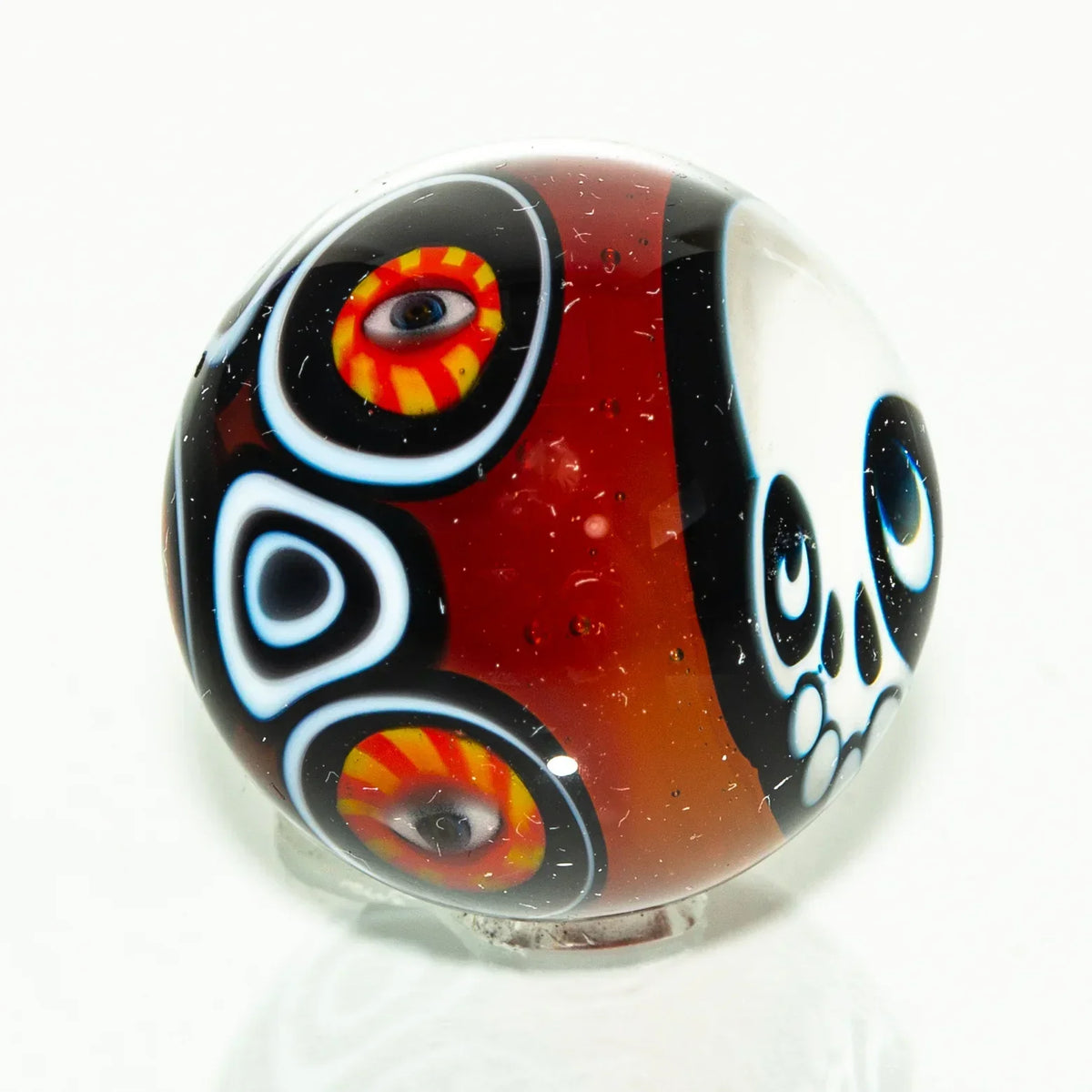 Handcrafted glass marble with skull and colorful eye designs on a red and black background