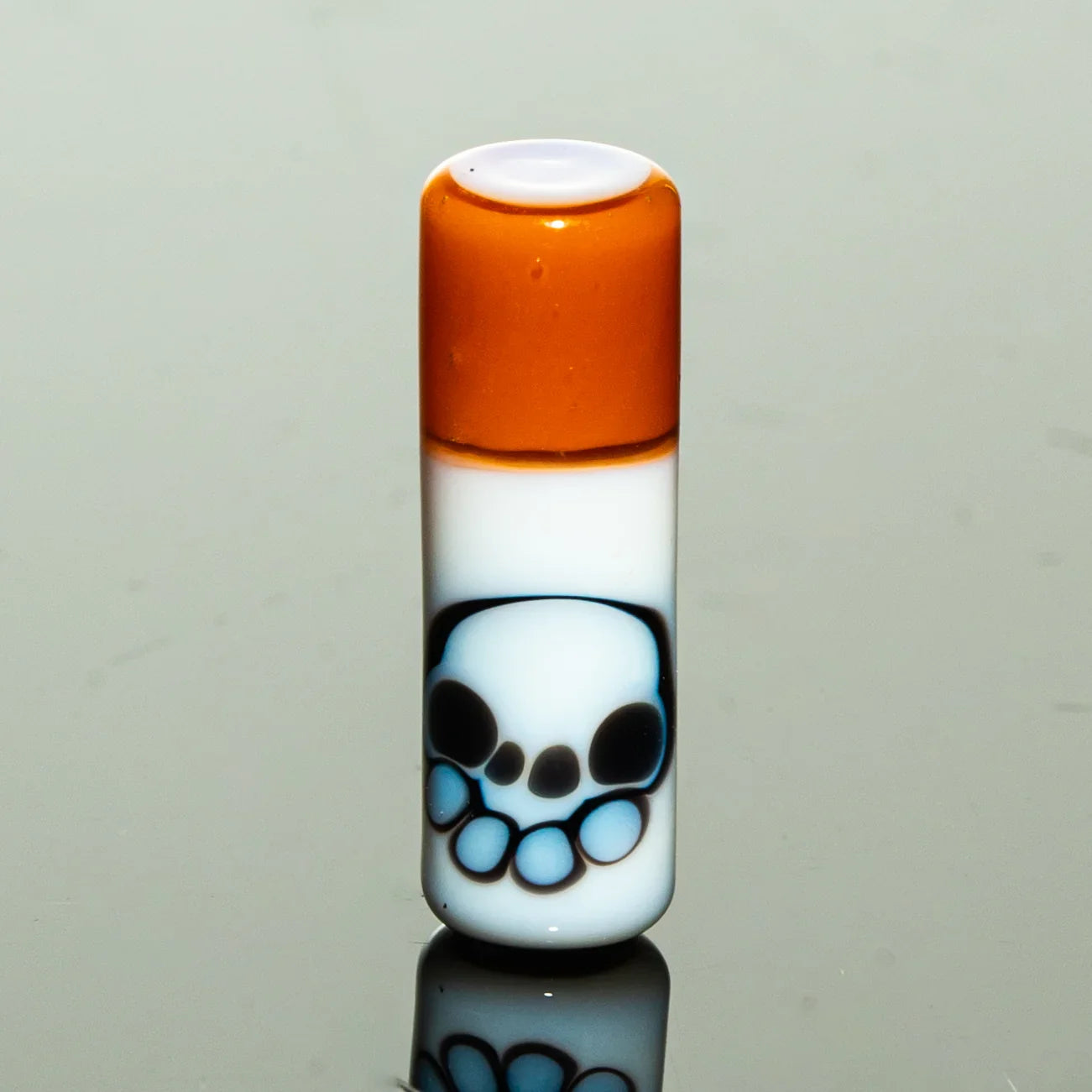 Hand-blown glass accessory with orange top and skull design on white background