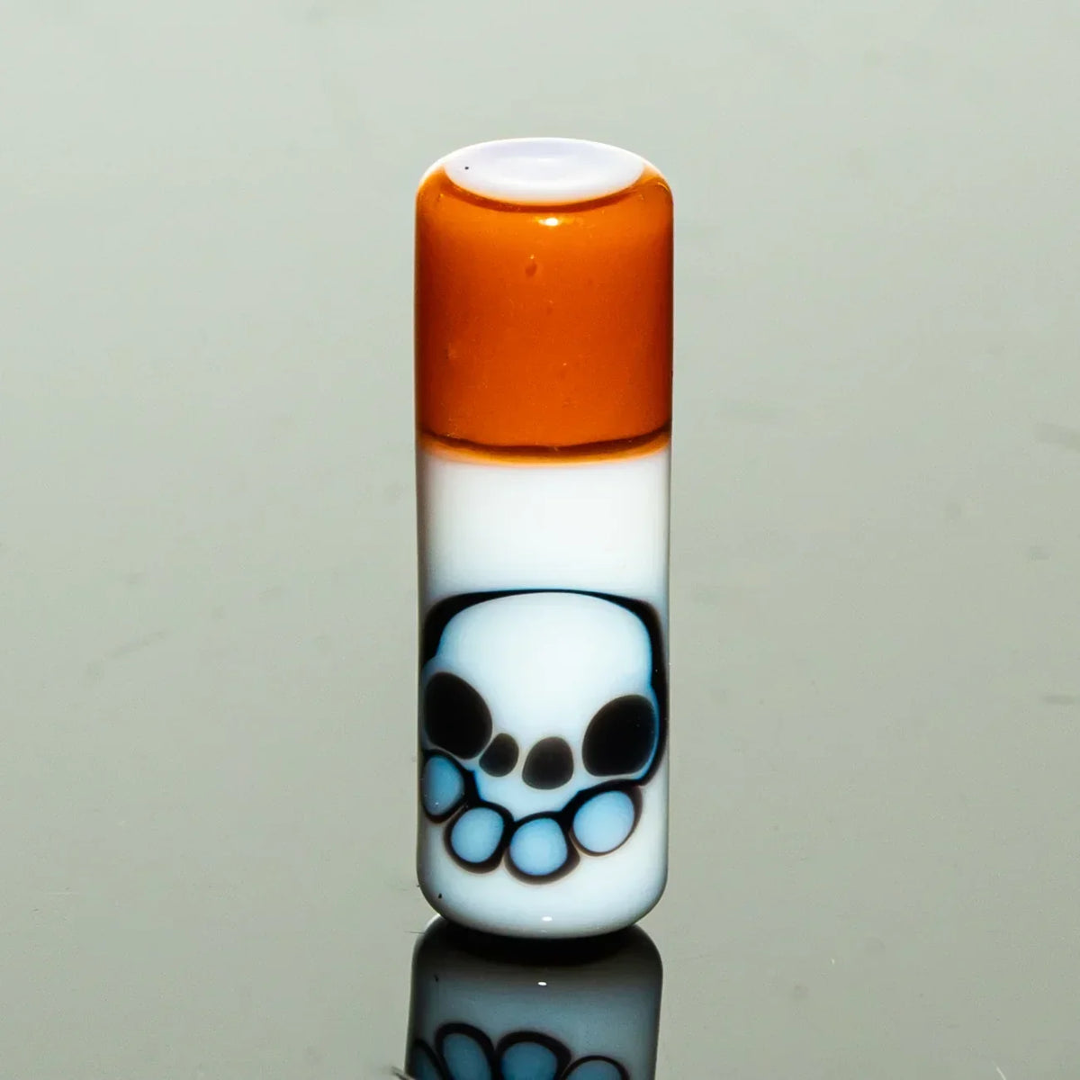 Hand-blown glass accessory with orange top and skull design on white background