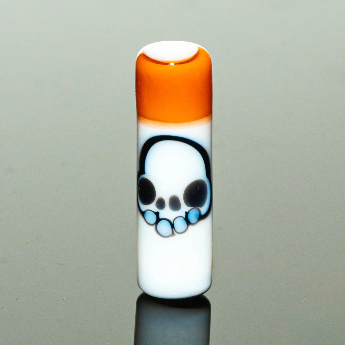 White glass accessory with orange top and blue skull design, reflective surface