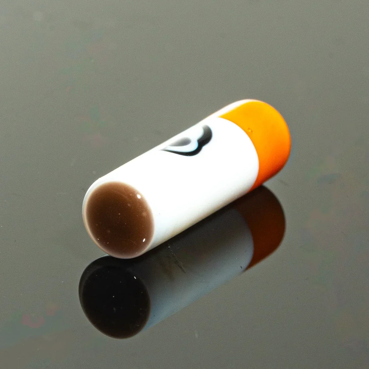 Glass cigarette one hitter bat with orange tip on black reflective surface
