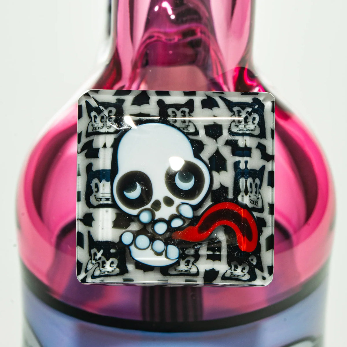 Close-up of colorful glass smoking accessory with cartoon skull design and pink background
