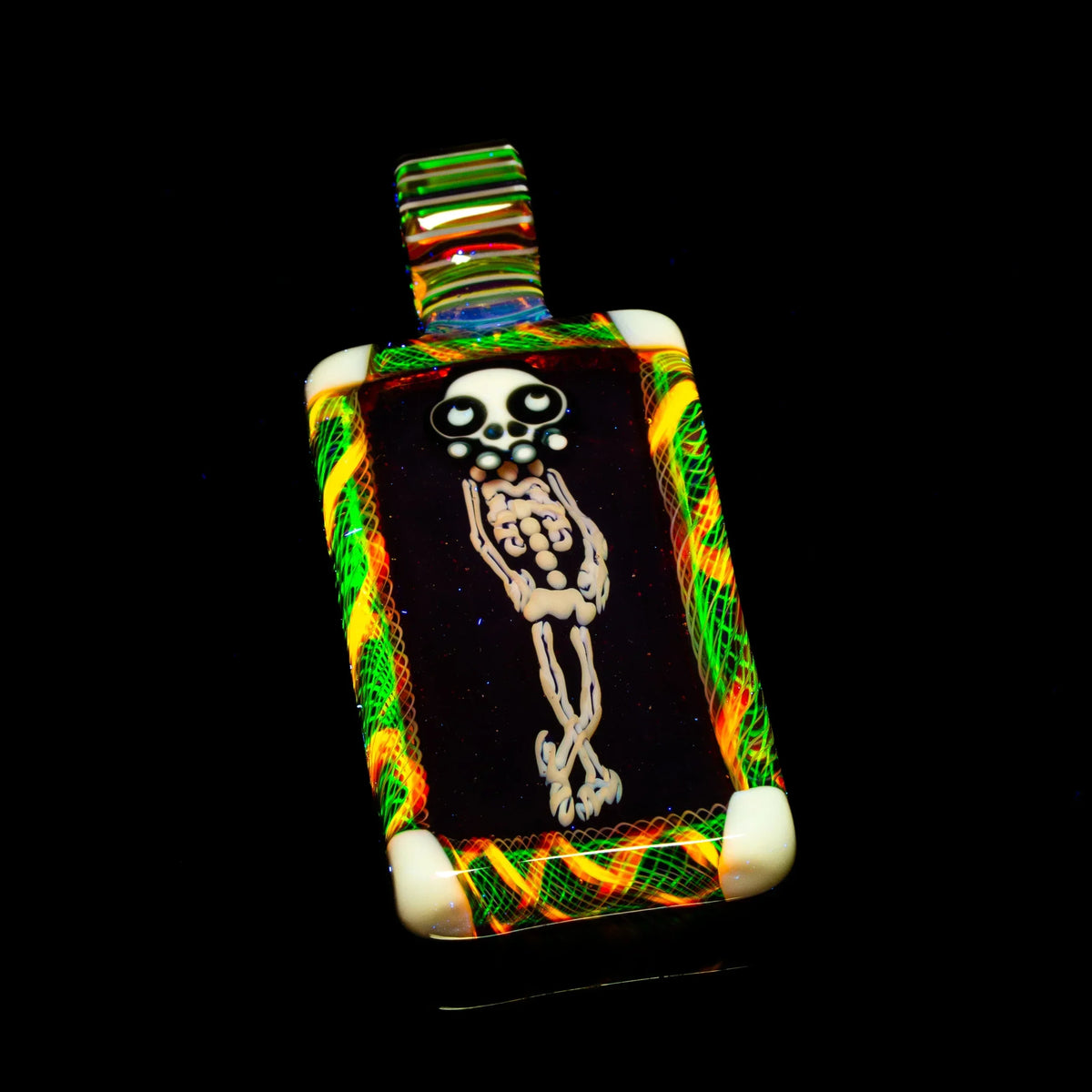Heady glass pendant with skeleton design, bordered by colorful patterns on black background