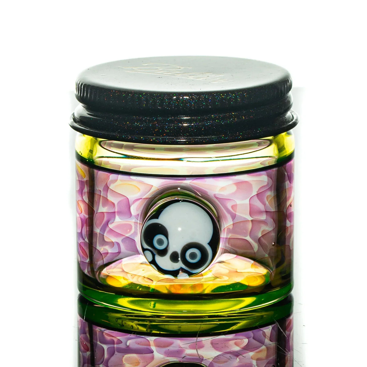 Colorful glass jar with skull design, pink and yellow accents, black lid, reflective surface