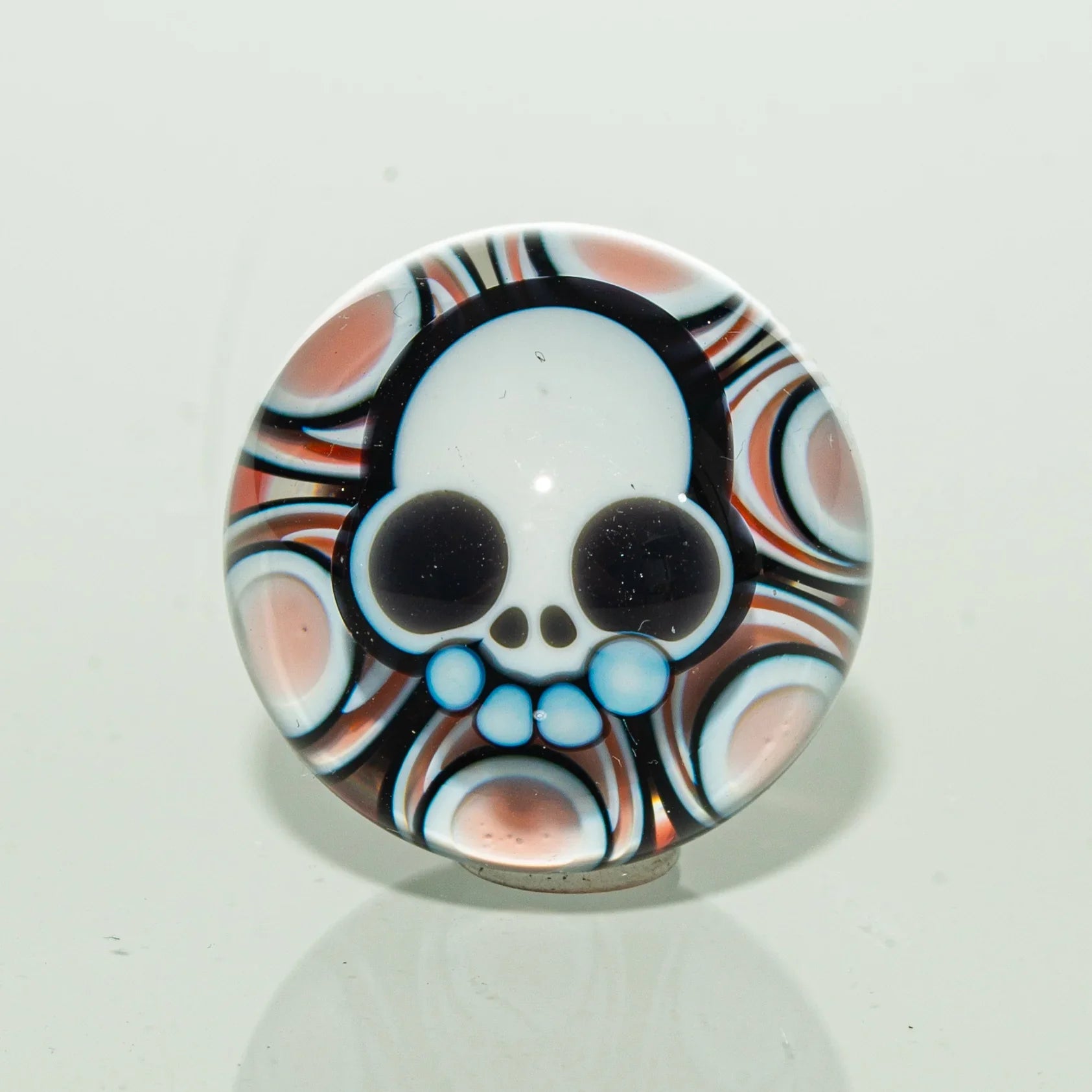 Colorful glass carb cap with a skull design and psychedelic pattern background.