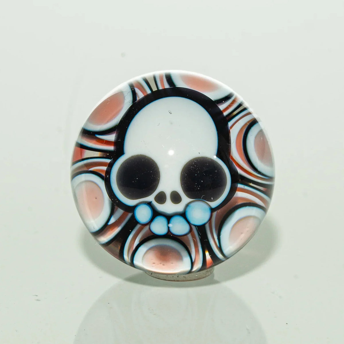 Colorful glass carb cap with a skull design and psychedelic pattern background.