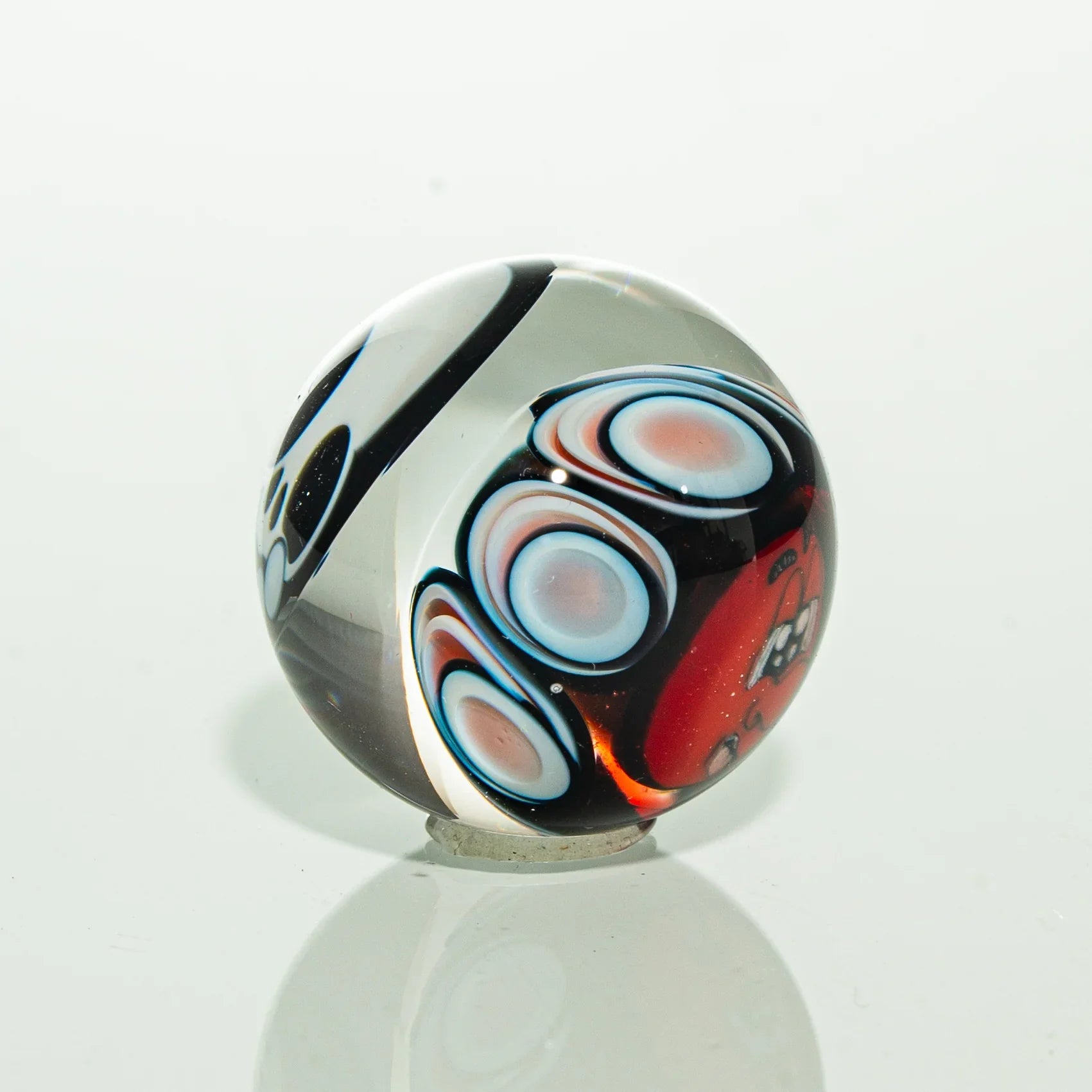 Handmade glass marble with colorful swirls and abstract red, blue, and black patterns