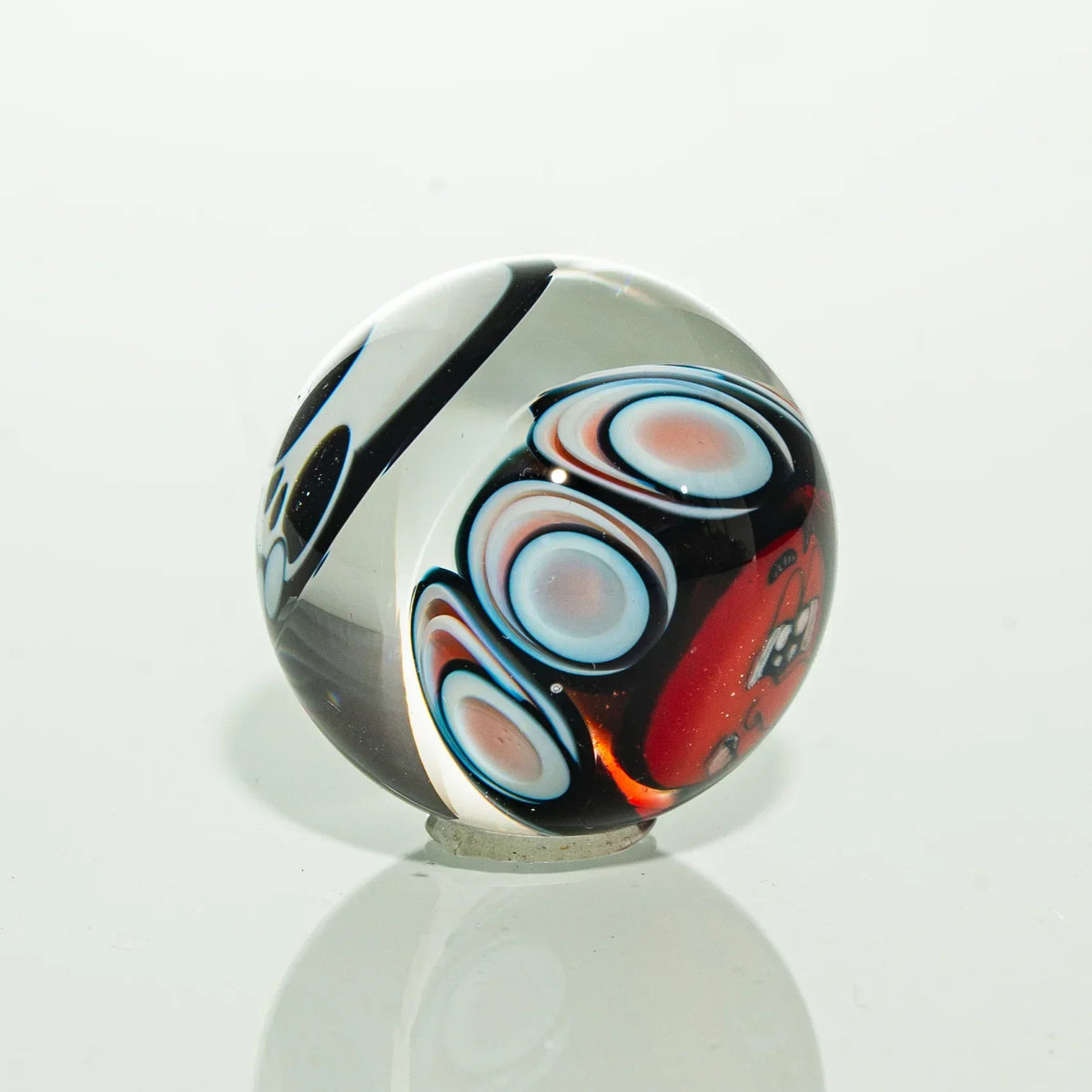 Handmade glass marble with colorful swirls and abstract red, blue, and black patterns