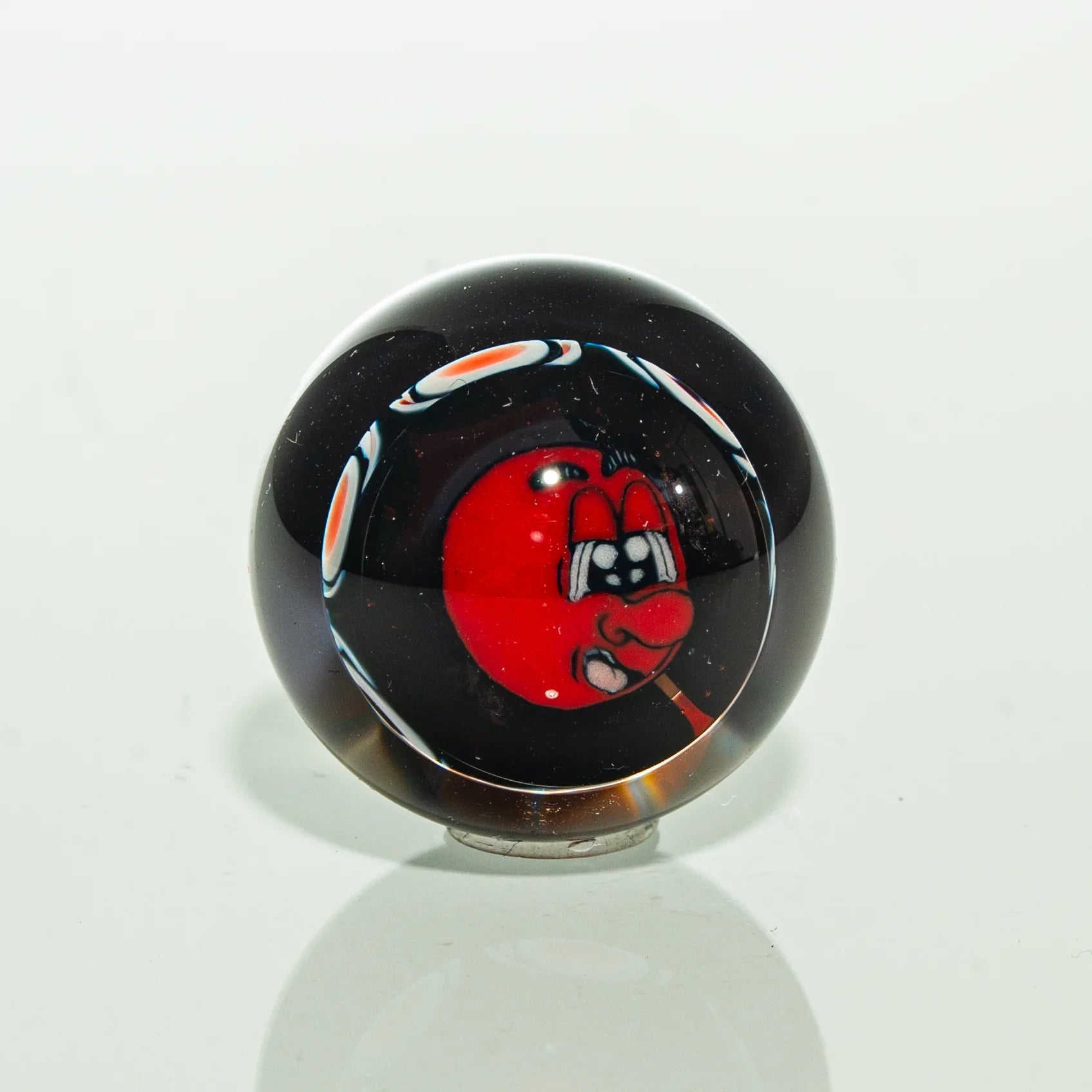 Handmade glass marble with vibrant red cartoon face design on black background
