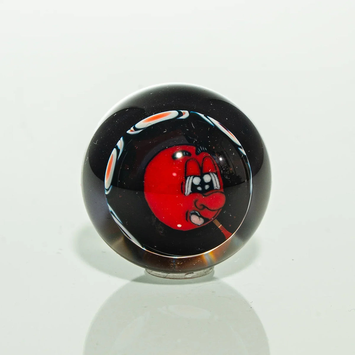 Handmade glass marble with vibrant red cartoon face design on black background