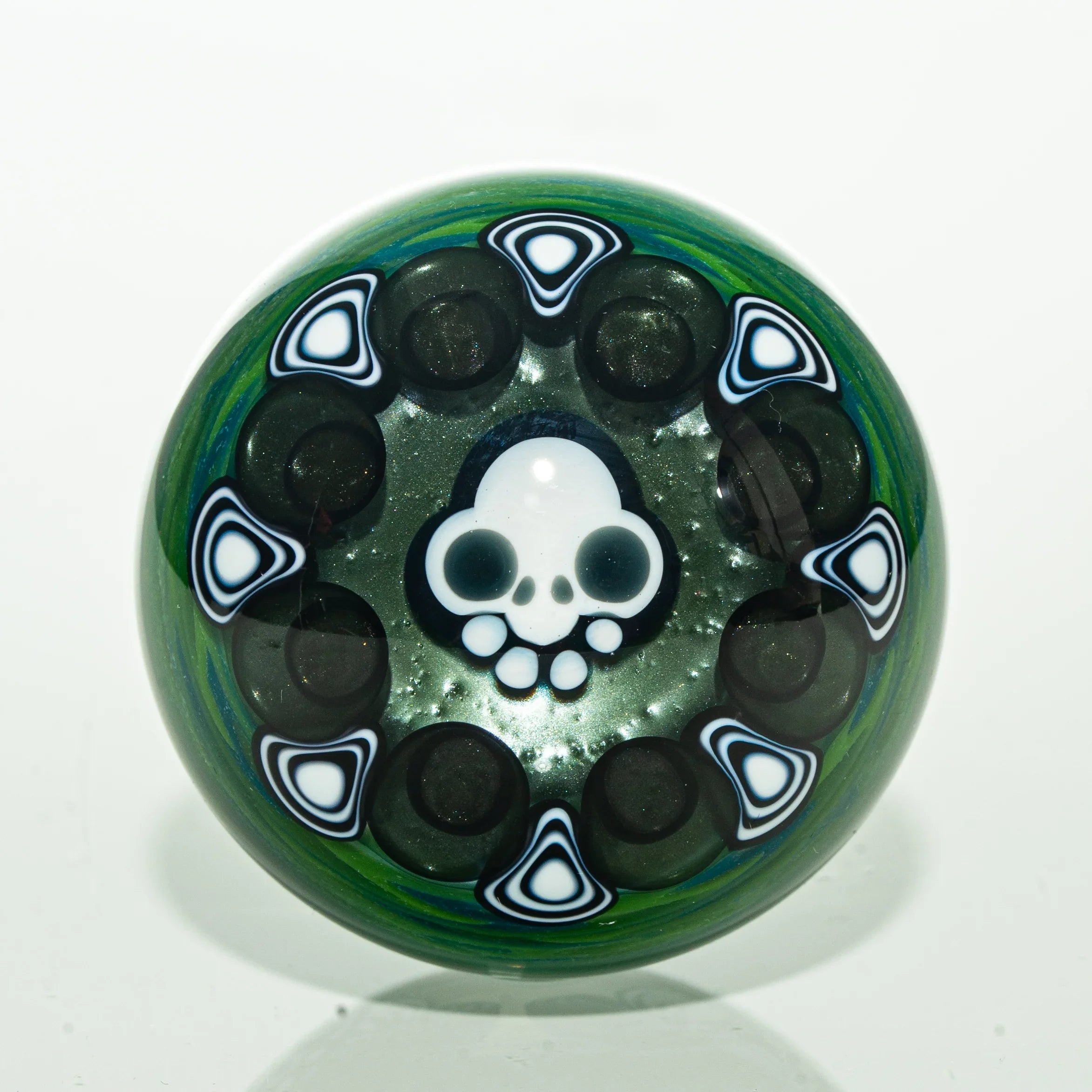 Handcrafted glass marble with skull design and black white accents on green background