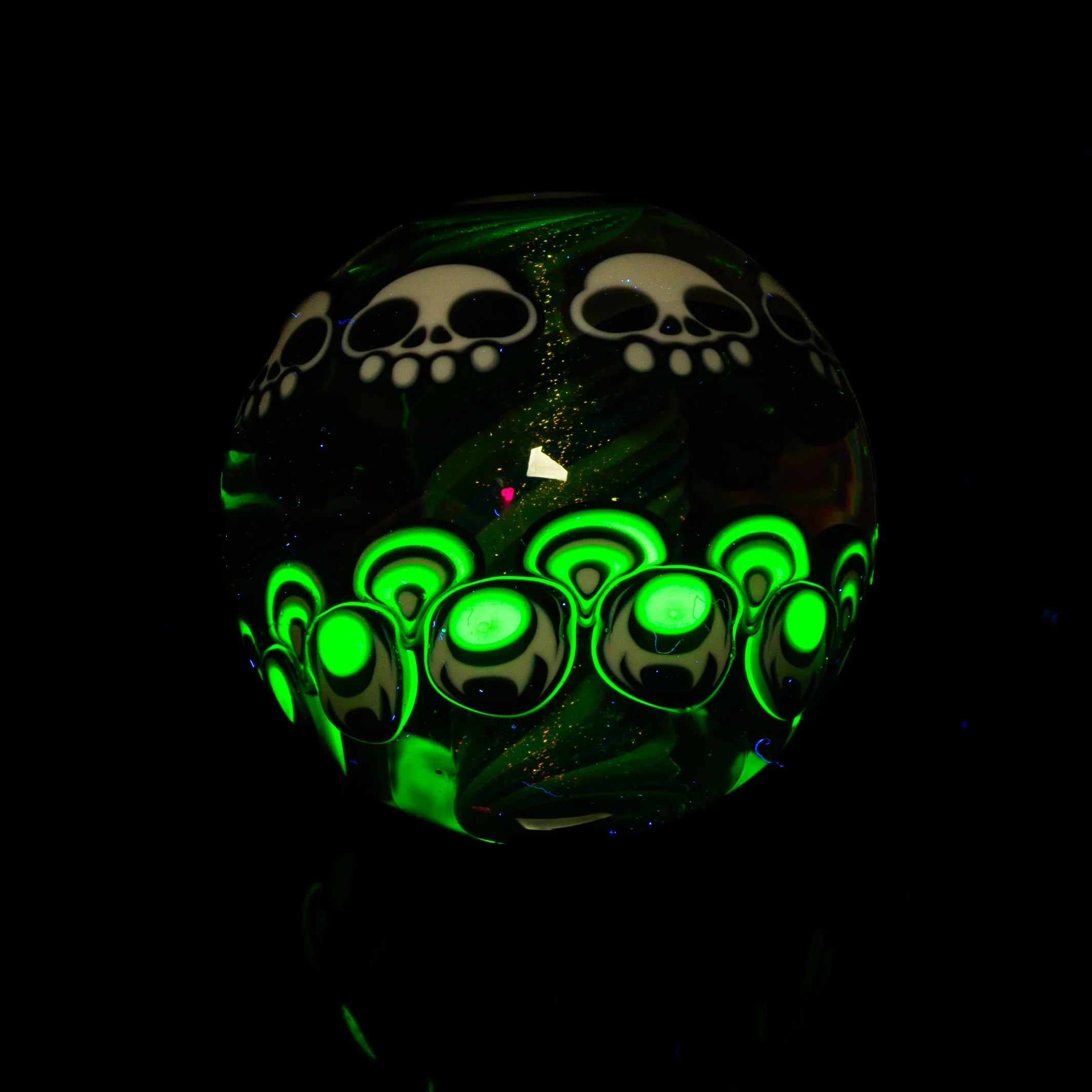 Glowing glass marble with neon green accents and skull designs against a black background.