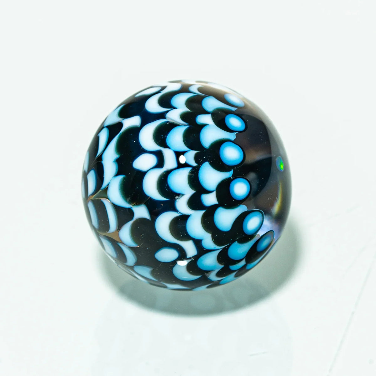 Handmade glass marble with blue and white scales pattern on a white background