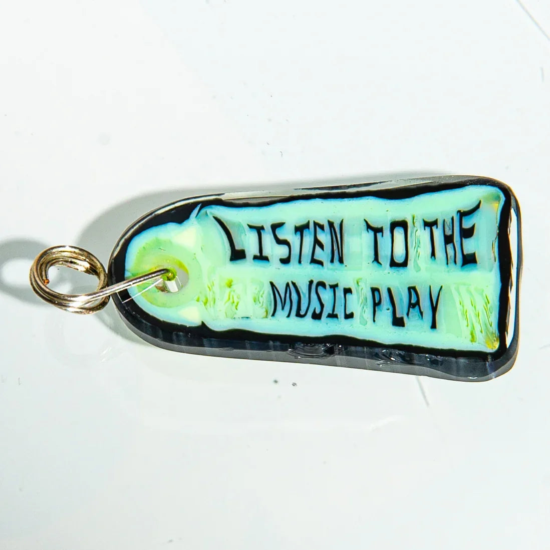 Handmade glass keychain with text 'Listen to the Music Play' on white background.