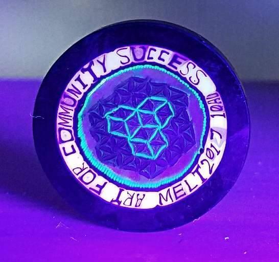 UV reactive glass token with geometric heart design and 'MELT 2017 ART FOR COMMUNITY SUCCESS' inscription