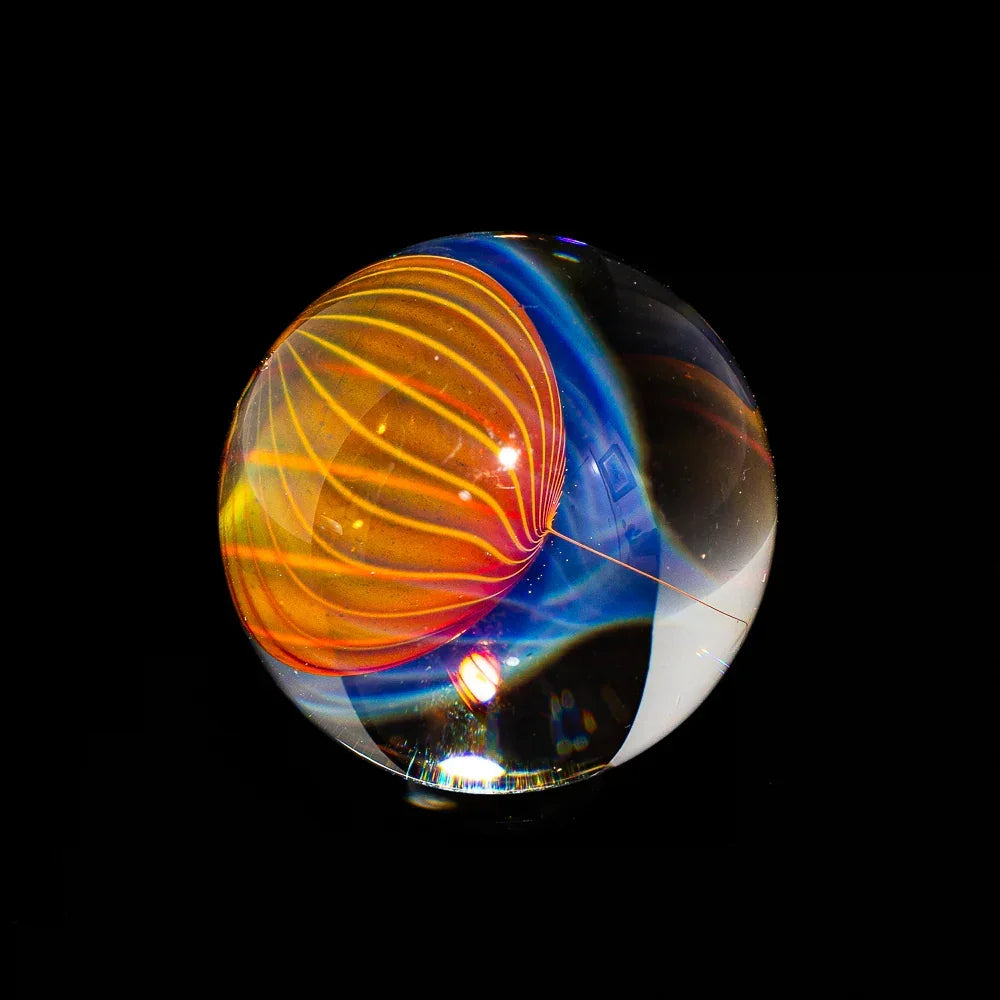 Handcrafted glass marble with vibrant orange and blue flame design on black background