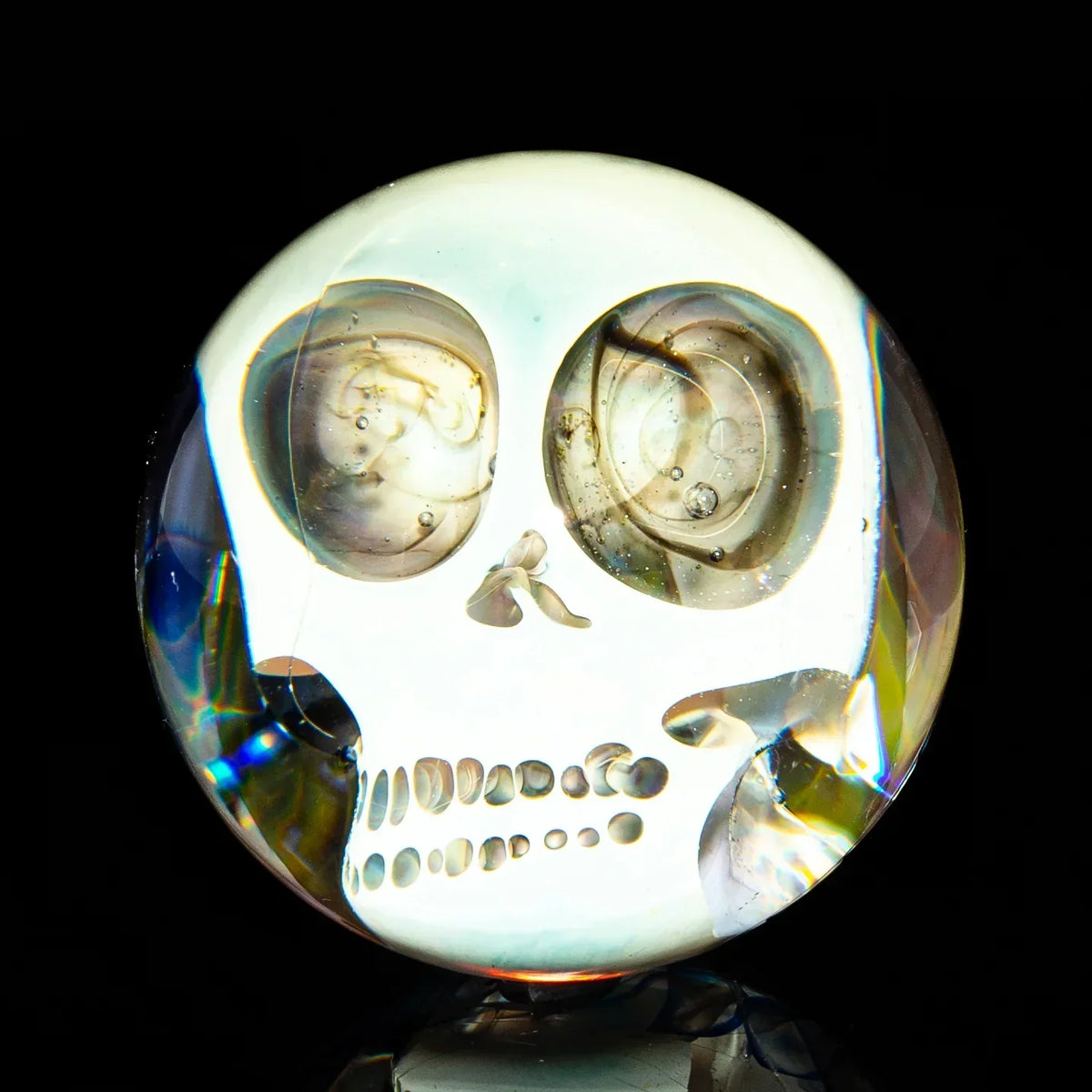 Clear glass marble with intricate skull design, heady glass art on black background