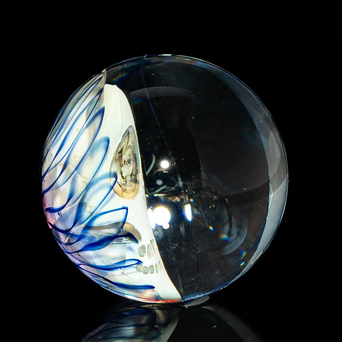 Hand-blown glass marble with clear orb and blue swirled accents on black background