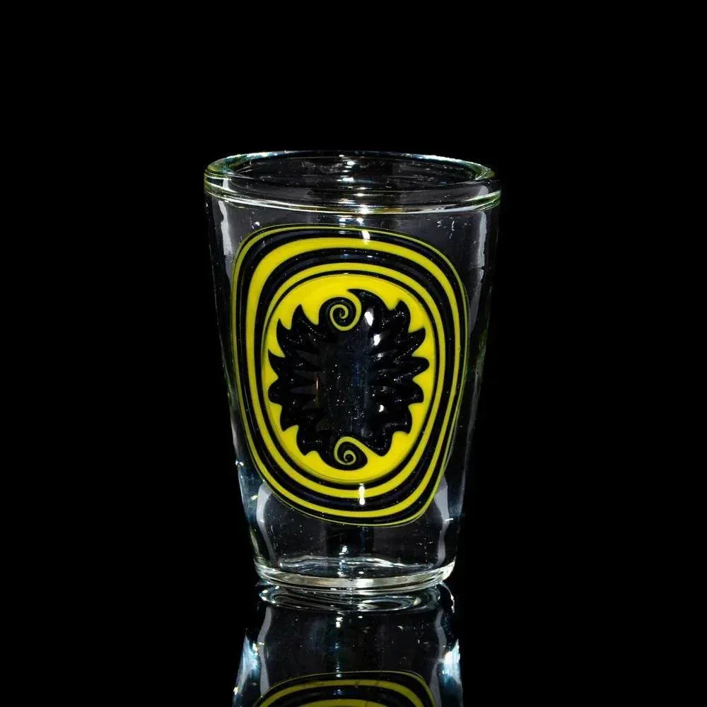 Artistic shot glass with black and yellow swirl design on clear glass, against black background