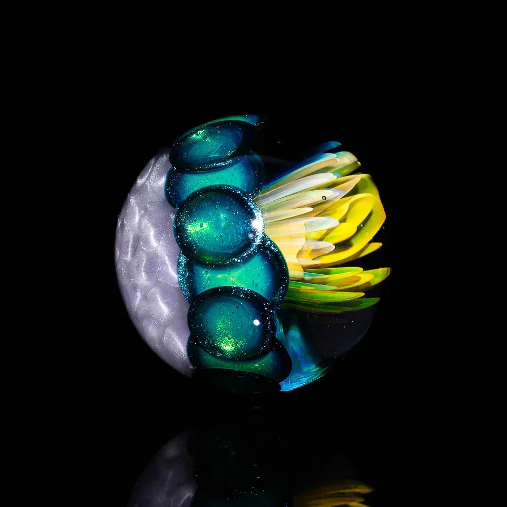 Handcrafted glass marble with blue orbs and yellow flower design on black background