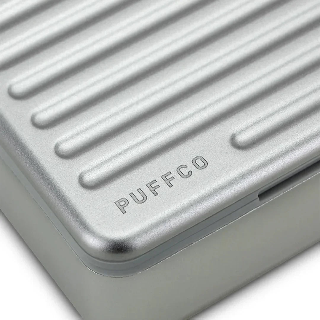 Close-up of a Puffco branded silver metal case with a ribbed textured lid.