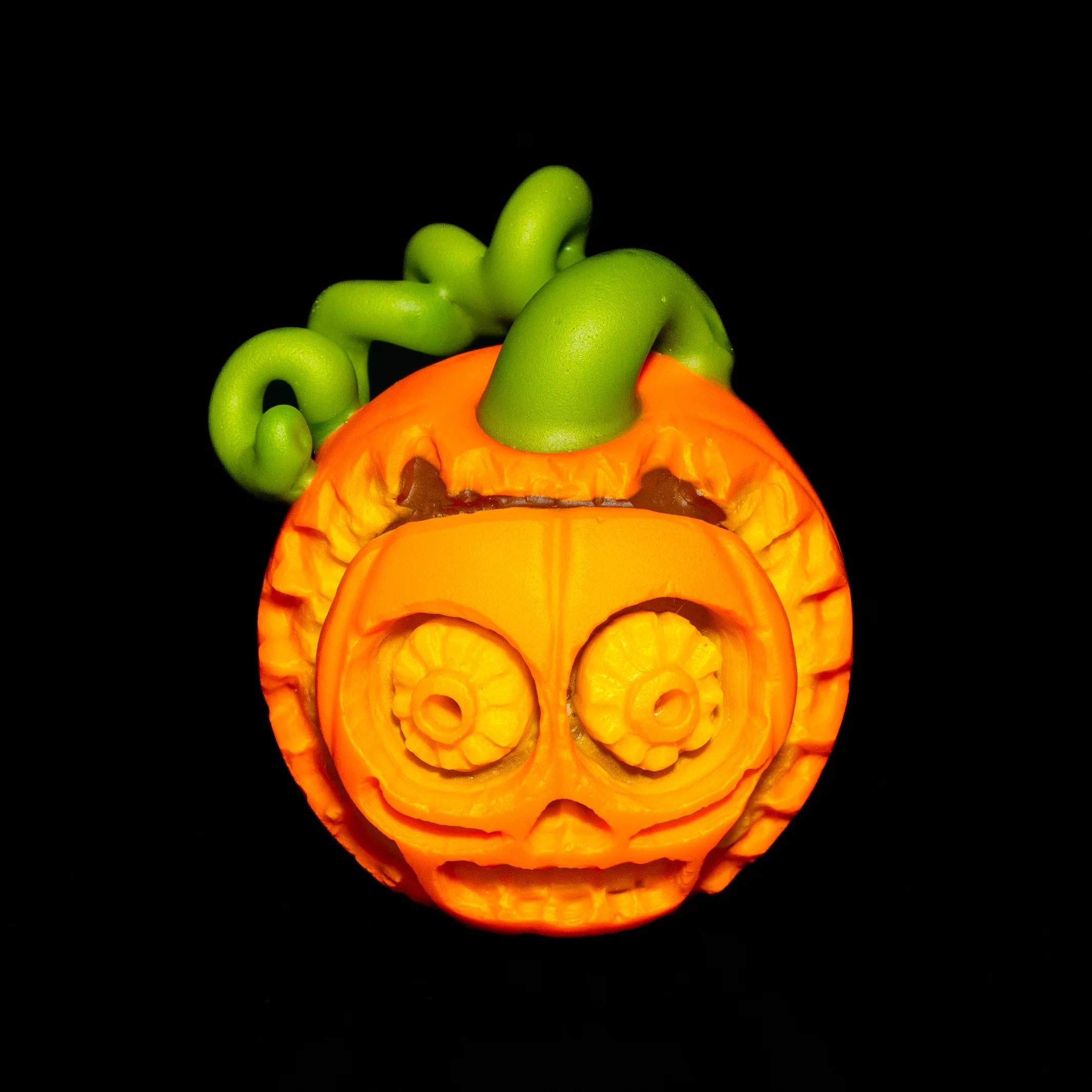 Handcrafted glass pumpkin pipe with detailed skull face and green stem on black background