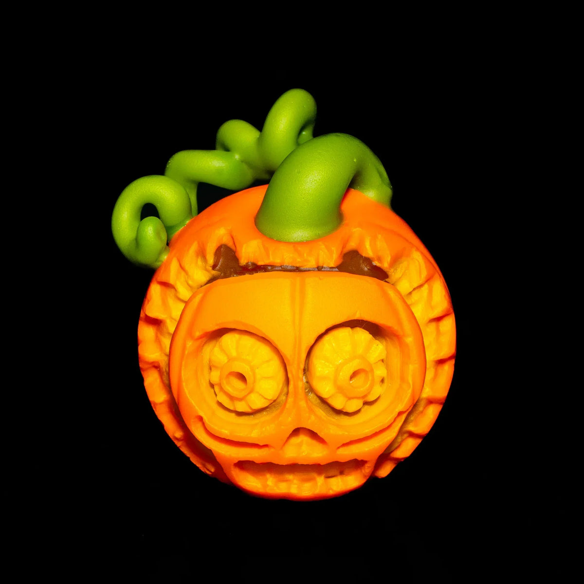 Handcrafted glass pumpkin pipe with detailed skull face and green stem on black background