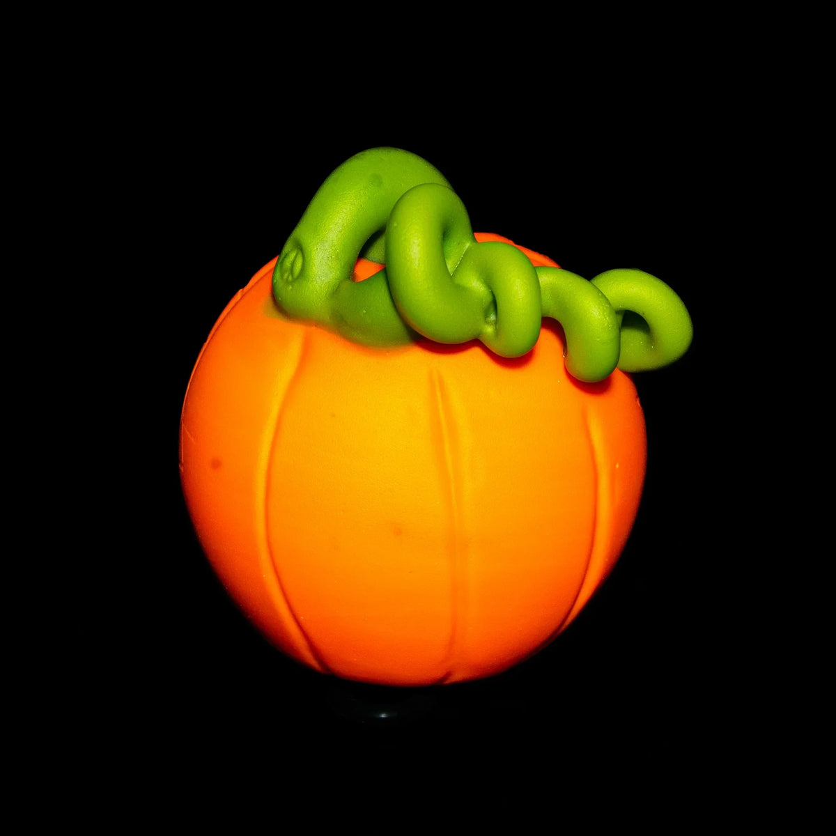 Handcrafted glass pumpkin pipe with bright orange body and green vine stem on black background.