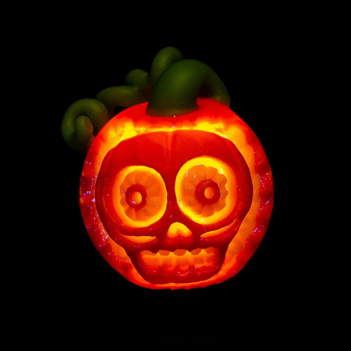 Glowing glass pumpkin with carved skull face and green stem on black background