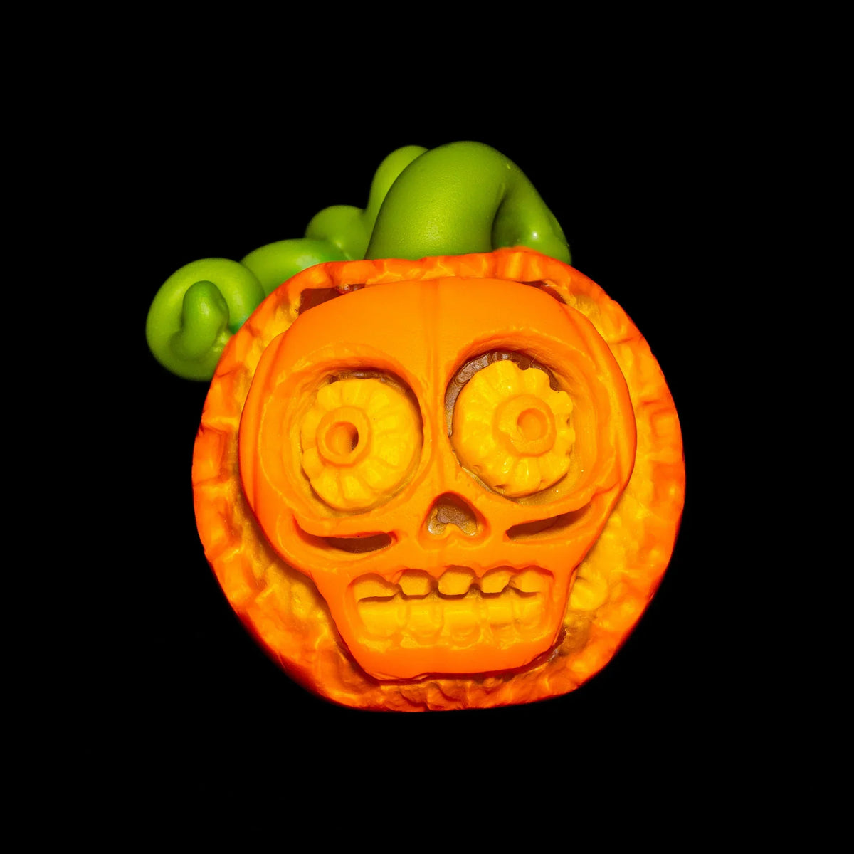 Handcrafted glass pumpkin with skull face and green stem on black background