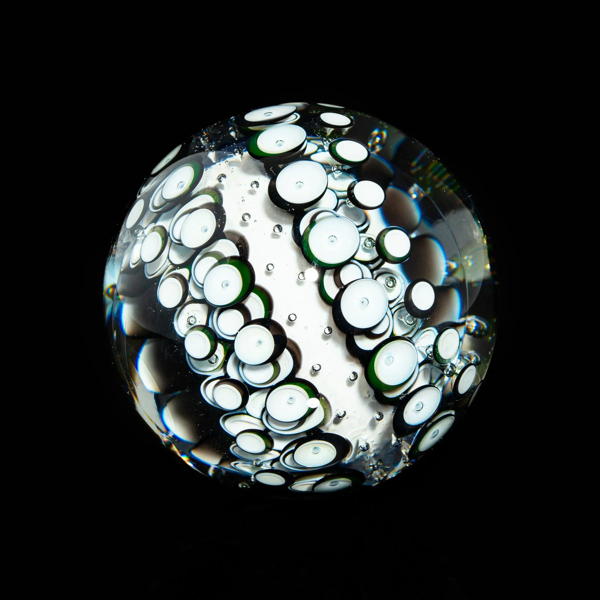 Handcrafted glass marble with intricate white and green bubble patterns on black background