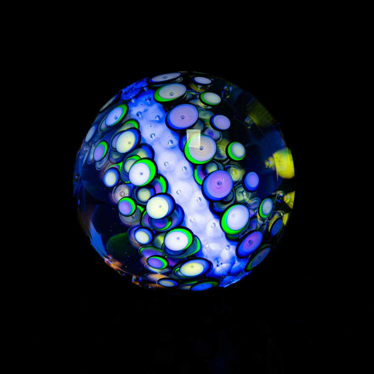 Handcrafted glass marble with blue, green, and purple swirling patterns on a black background