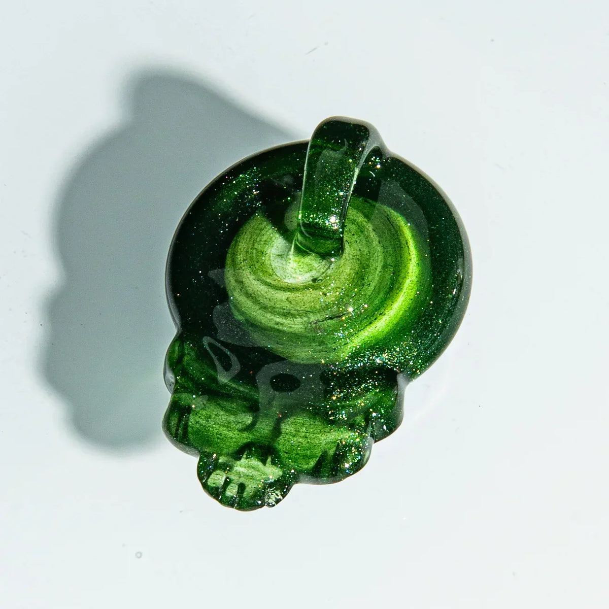 Green glass pendant shaped like a skull with a loop, displayed on a white background.