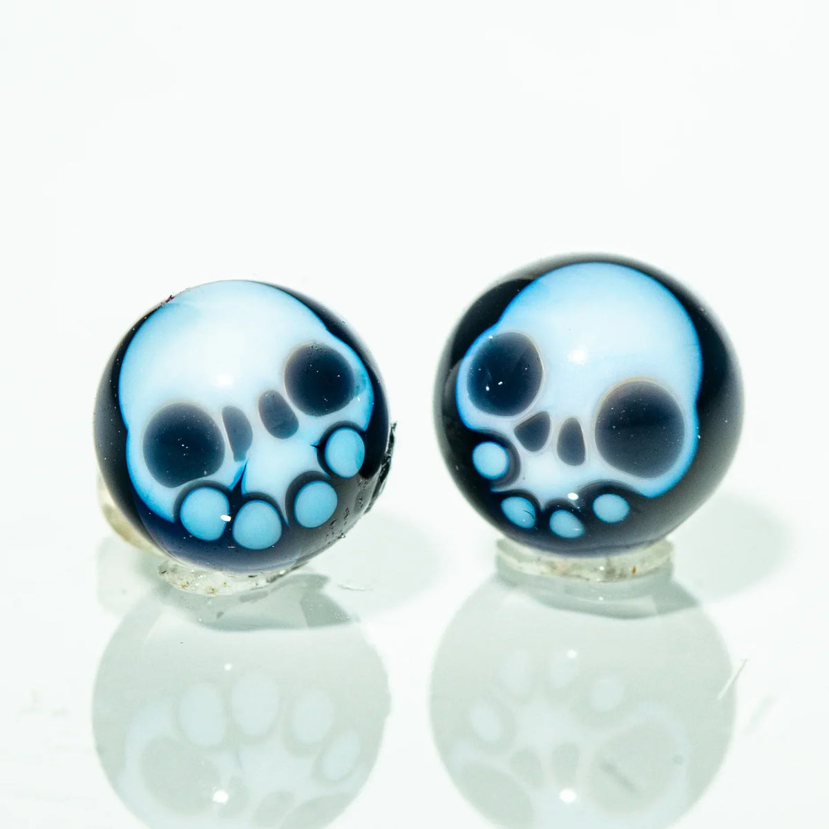 Two glass skull terp pearls with blue and white design on a reflective surface