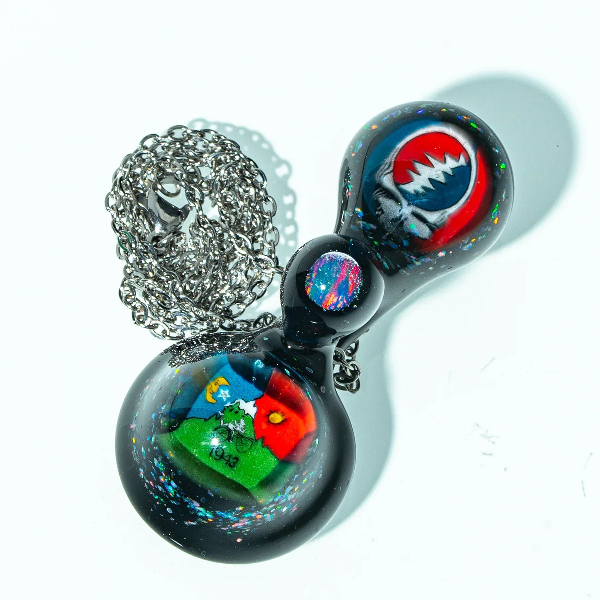 Colorful glass pendant necklace with artistic designs and metallic chain on white background.