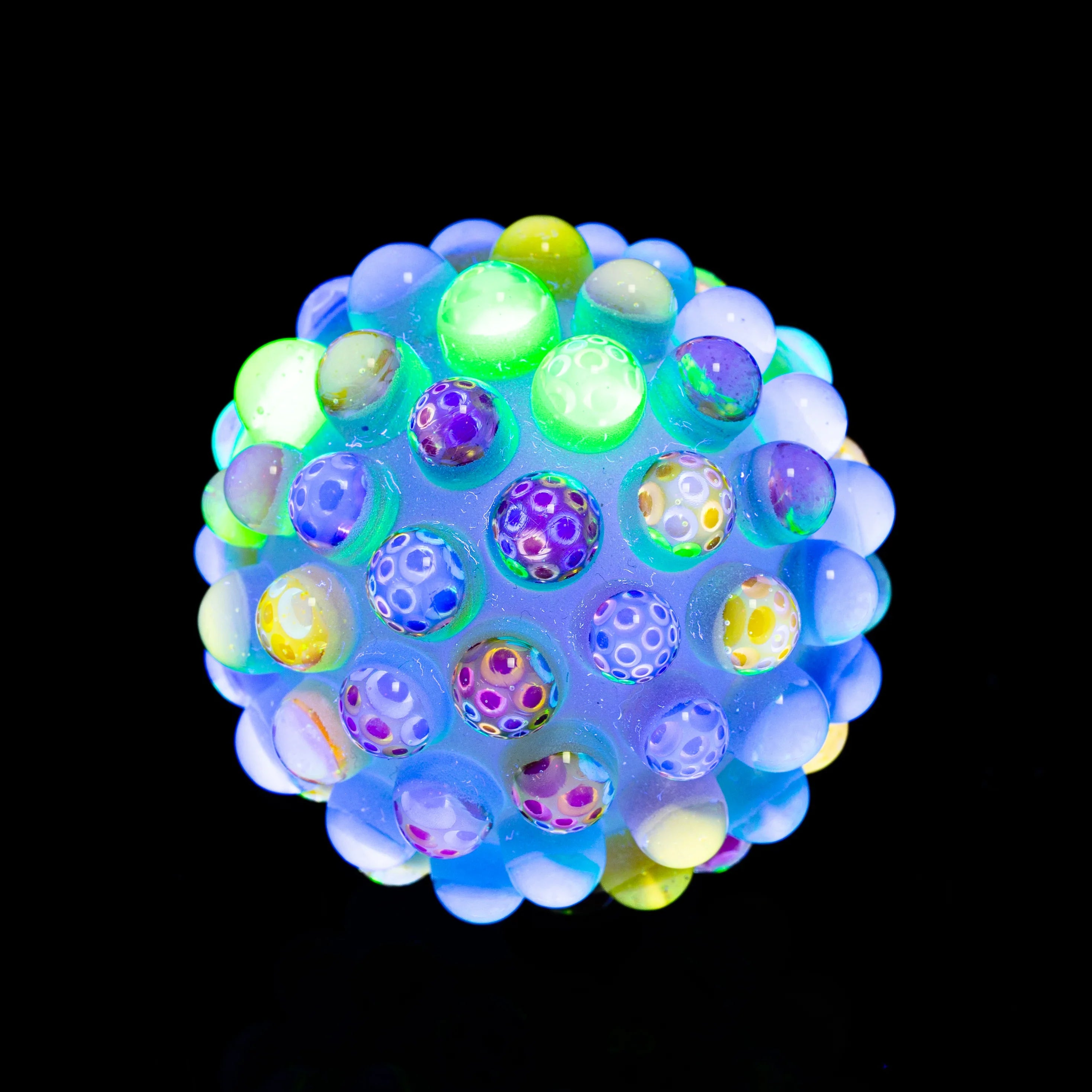 Colorful heady glass sphere with raised dots, glowing under blacklight on black background